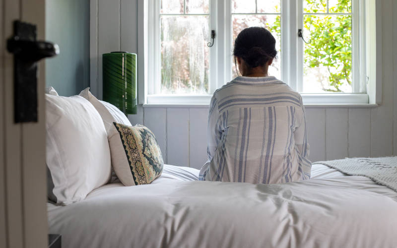 A photo of a high-functioning depressed person sitting on a bed and looking out a window.